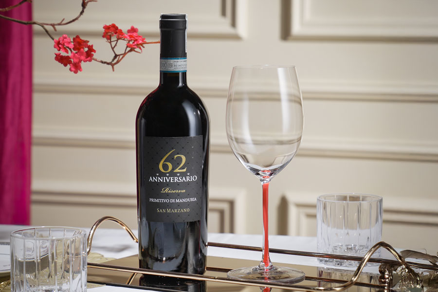 Chai Anniversario 62 San Marzano với thiết kế nhãn cổ điển, đặt cạnh hình ảnh 19 người nông dân đang làm việc hoặc logo kỷ niệm 62 năm.